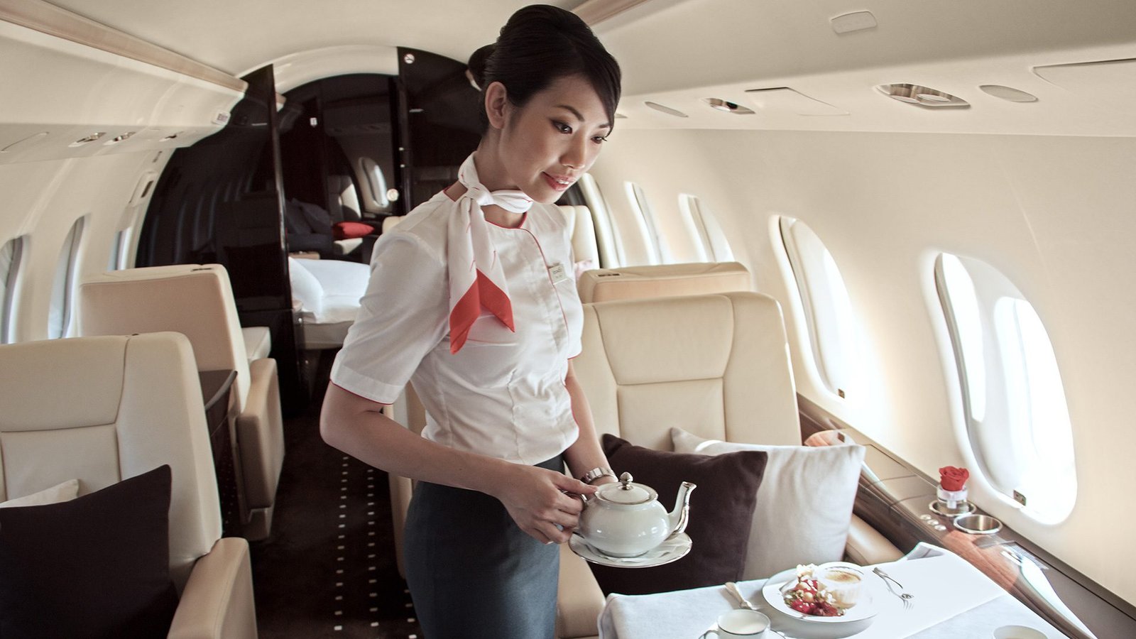 Professional cabin hostess providing exceptional personalized service with a warm smile aboard a private jet charter flight in East Asia