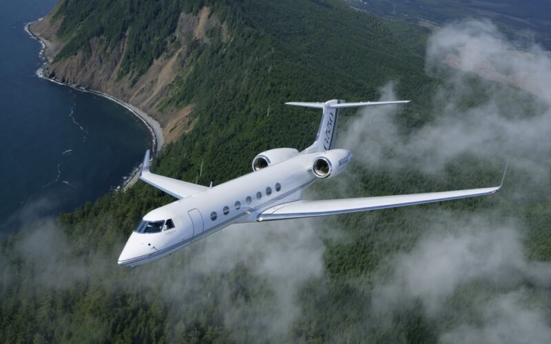 Gulfstream G550 business jet in flight over a forested coastline