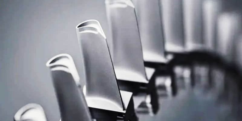 Extreme close-up of jet engine high-pressure turbine blades showing single-crystal construction, golden ceramic thermal barrier coating, visible cooling holes, and complex aerodynamic profiles