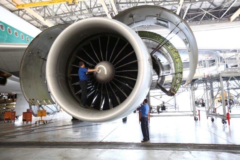 Engineer inspecting the fan of a large turbofan engine installed on an aircraft inside a maintenance hangar