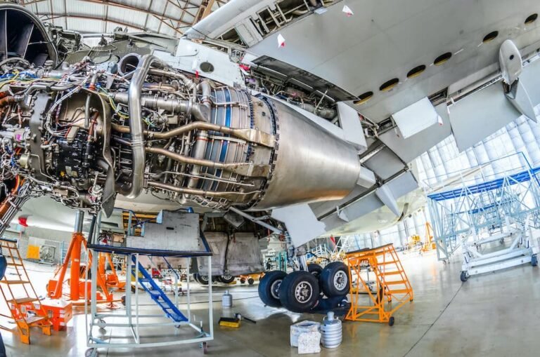 Large turbofan engine opened up for maintenance in an aircraft hangar, with access stands and a wide-body aircraft behind it